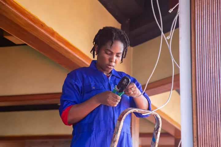 Eletricista de uniforme azul passando fiação no teto de uma casa