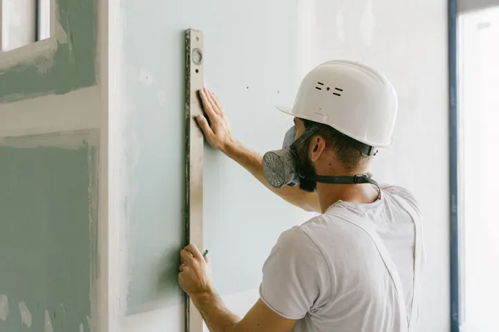 Profissional de capacete conferindo o nível de uma parede de drywall